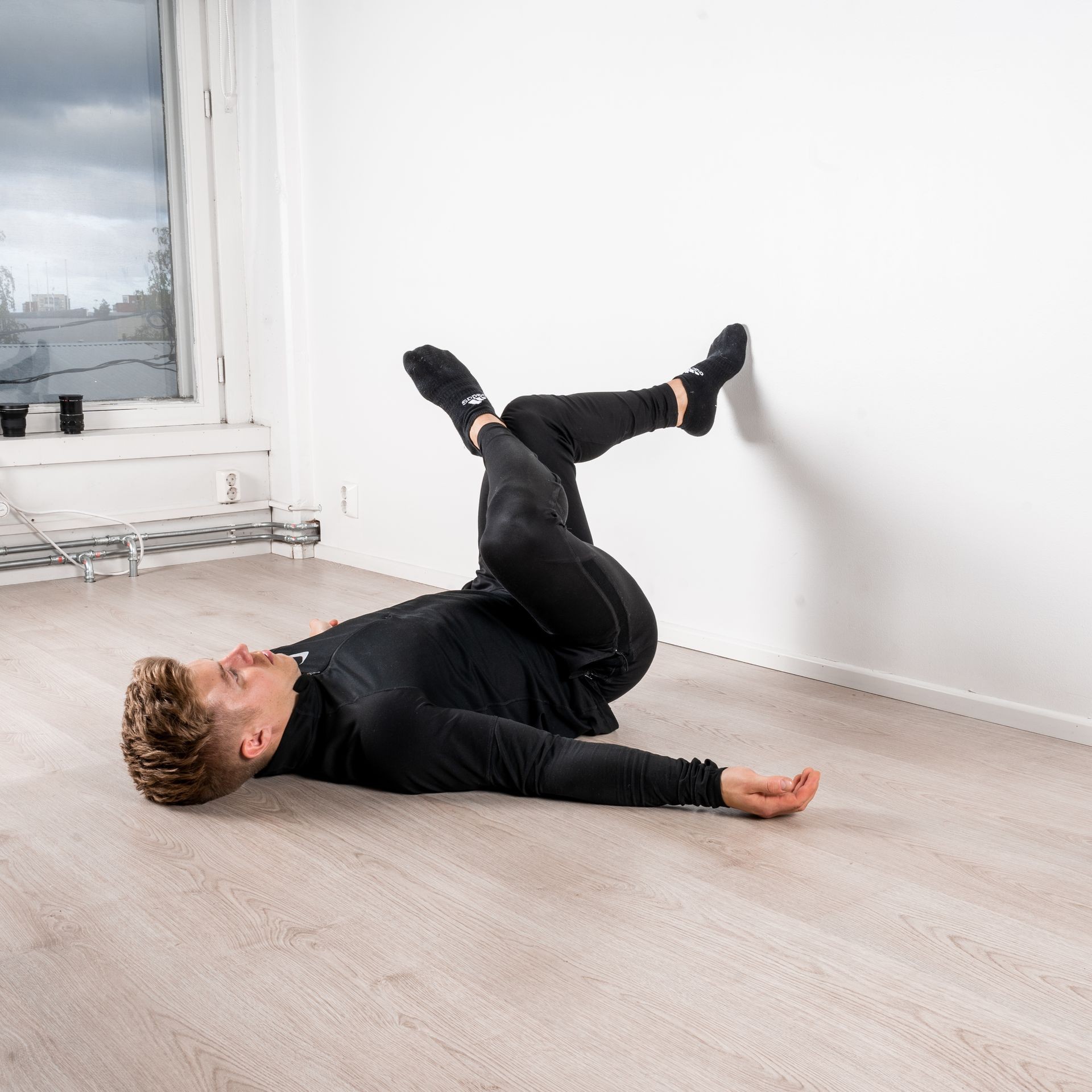 Person in black workout attire performing a leg stretch with feet on the wall.